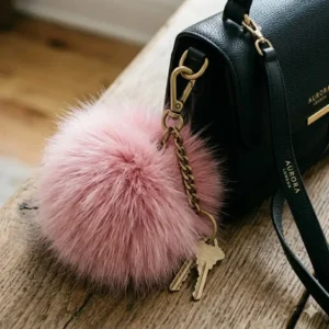 A soft pink fluffy pom-pom keychain big decorative accessory on a black handbag.