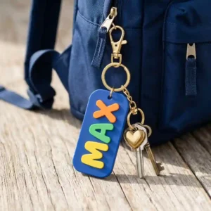 A durable blue plastic key chain with name attached to the zipper of a school backpack.