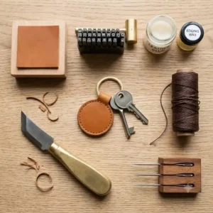 A flat-lay illustration of the tools used to make a genuine leather key ring, including a cutting knife, thread, and needle.