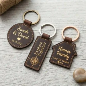 A tight square illustration displaying multiple custom engraved keychains with tactile, deep laser-engraving on quality brown leather tags, featuring classic fonts, gold-leaf accents, a compass motif, and a couples theme.