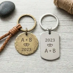 A high-resolution, top-down square photograph featuring matching custom engraved keychains for a couple, side-by-side on light wood with interlocking heart designs and engraved anniversary dates.